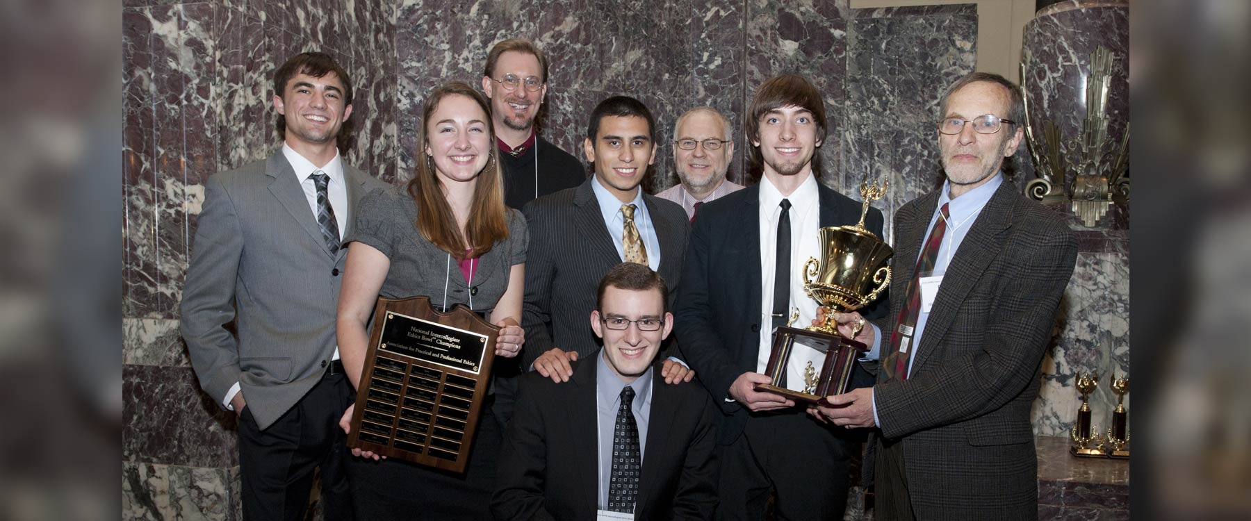Forensics students and coaches pose for a group photo. Two students hold up a trophy and plaque.