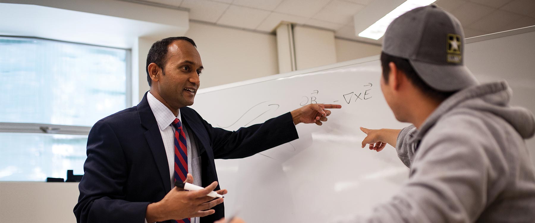 Professor Kamesh Sankaran stands across from a biophysics student talking. Both point toward an equation on a whiteboard.