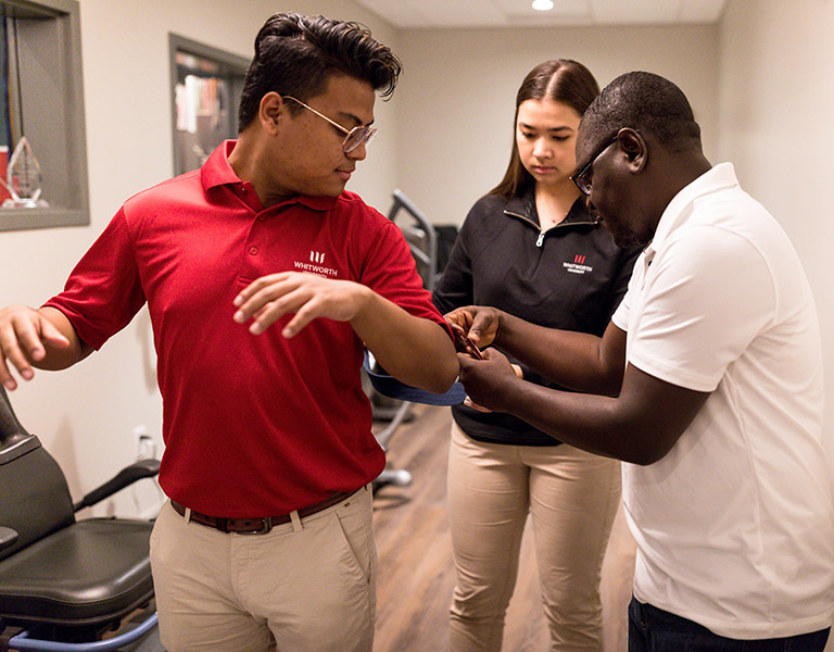 Two students practice applying a brace or sling to an instructors arm.