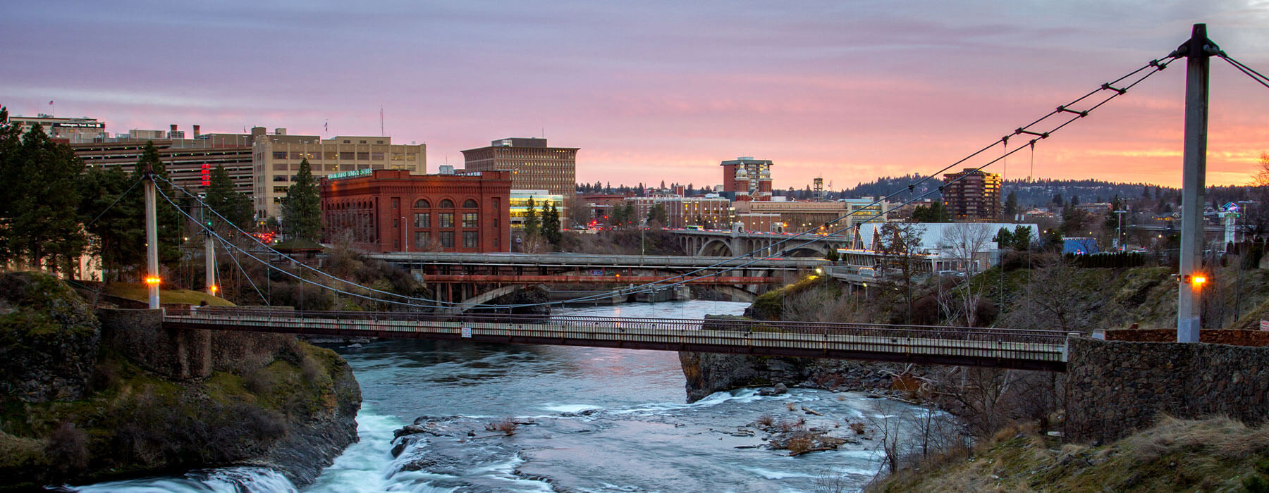 Cityscape at sunset with bridges over a river, buildings and a sky with pink hues.