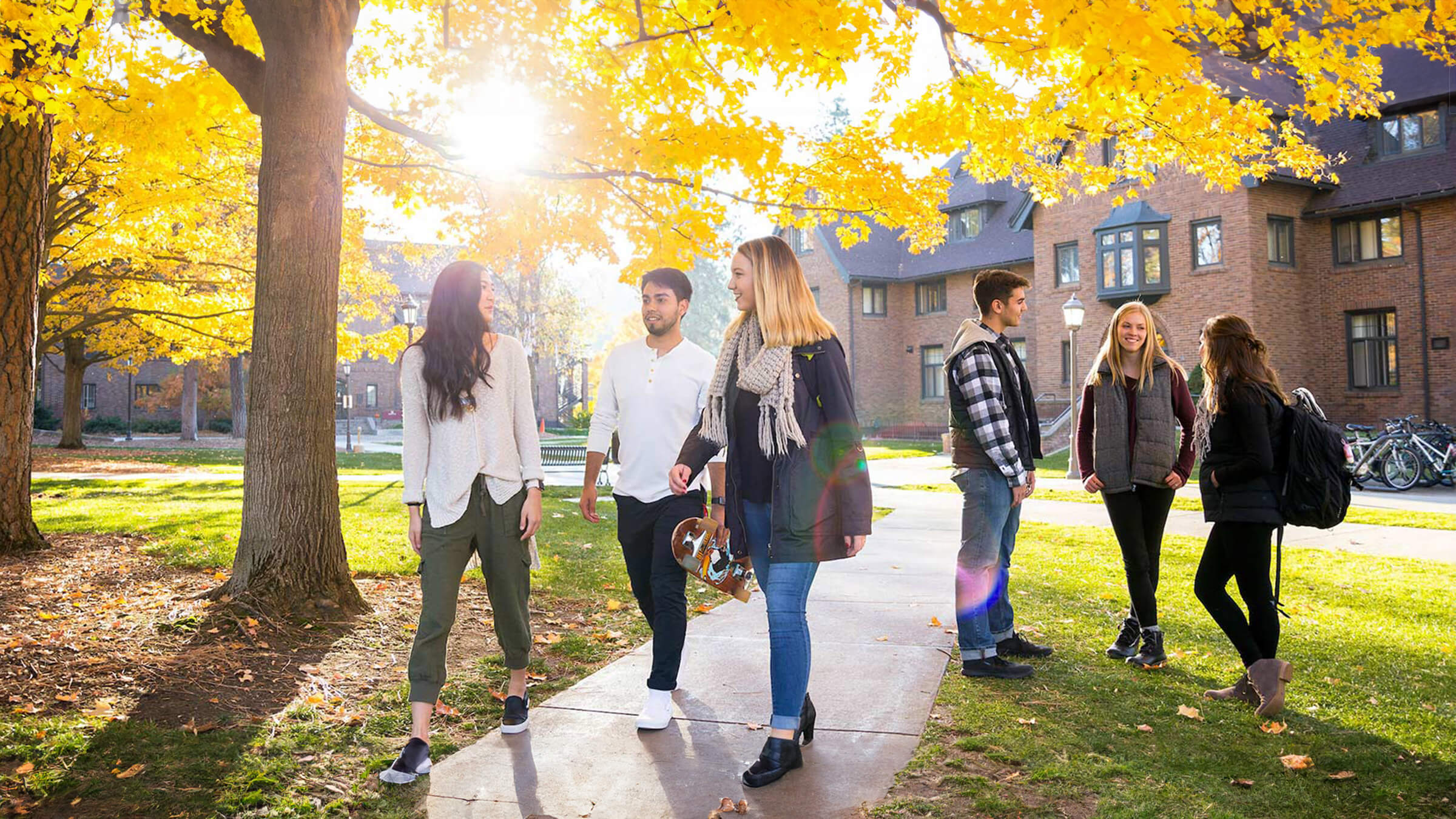 One group of three students walks down a campus path while another group stands, conversing.