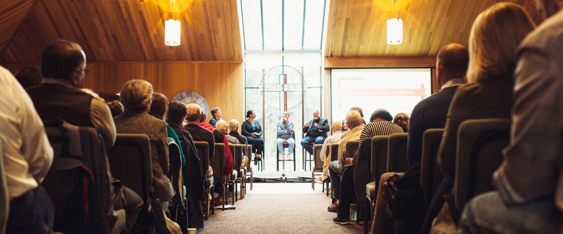 A panel of speakers sits at the front of the university chapel. The rows of seats are filled with listeners.