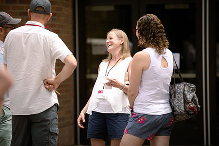 Four people chat and laugh together outside a building on a sunny day.