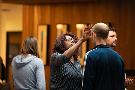 In an indoor church setting, one person anoints another, touching their forehead.