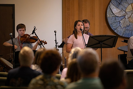 Musicians perform on stage in front of an audience in a church setting.