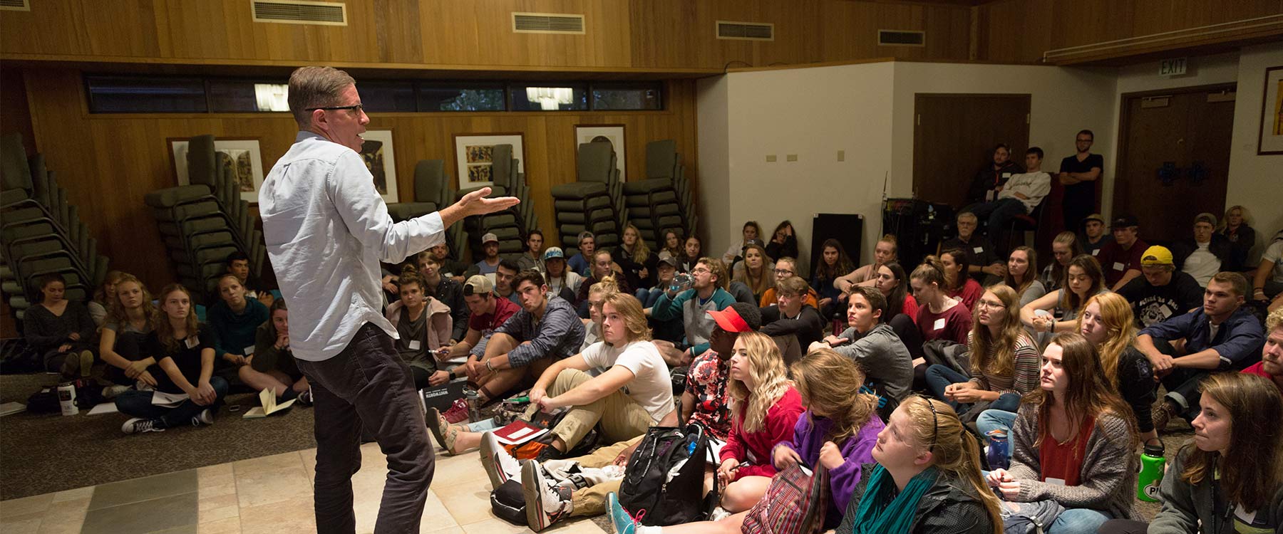 Kent McDonald speaks in front of a large group of students seated on the floor.