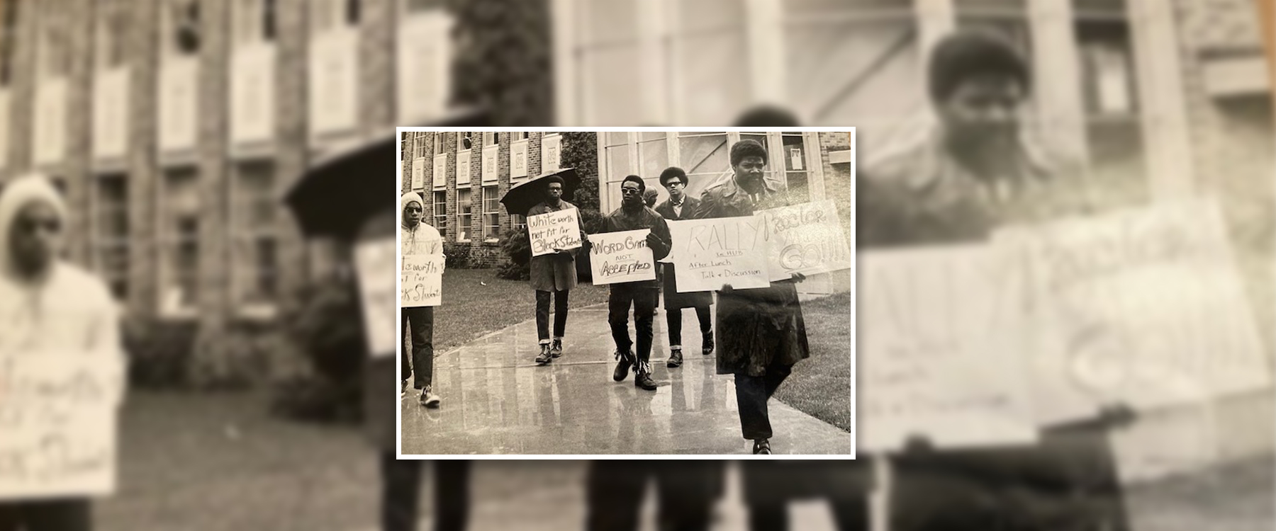 People marching outdoors, holding signs advocating against racism and calling for a rally.