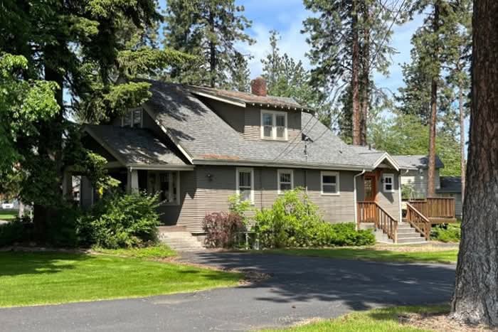 Street view of classic gray house with a lush front lawn, covered porch, and steps to a side entry and deck.