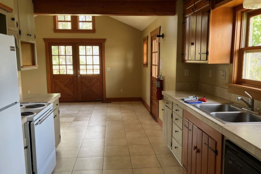 A spacious kitchen with wooden cabinets, tile floors, white appliances and double doors leading outside.