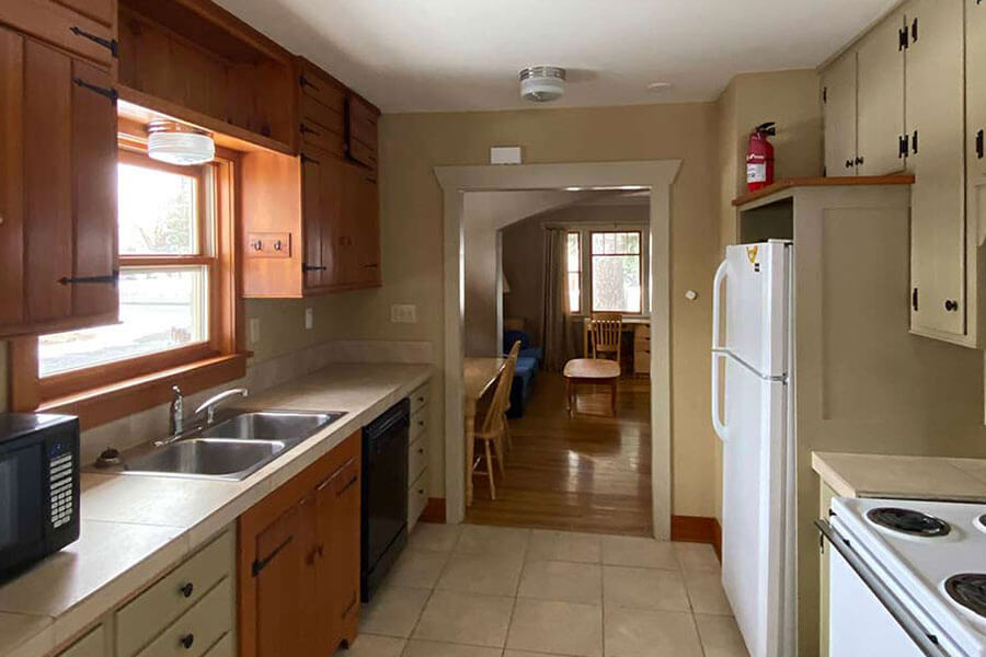 A large kitchen with wooden cabinets and full-size fridge, stove and sink. Dining area is visible through an open doorway.