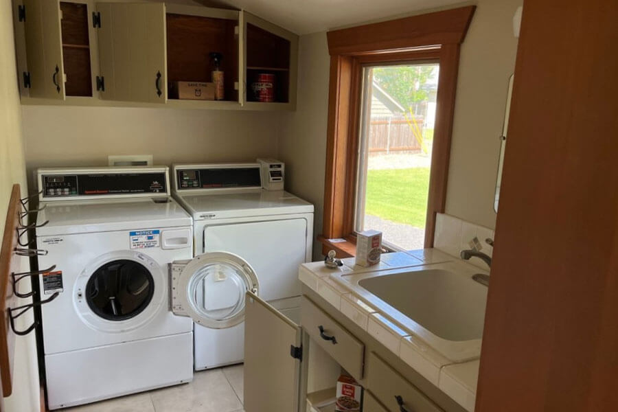 Laundry room with washer, dryer, sink, cabinets and a window overlooking a grassy yard.