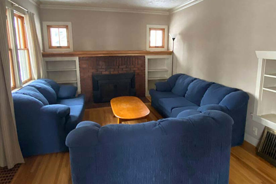 Living room with three blue sofas, a wooden coffee table, and a brick fireplace flanked by built-in shelves.