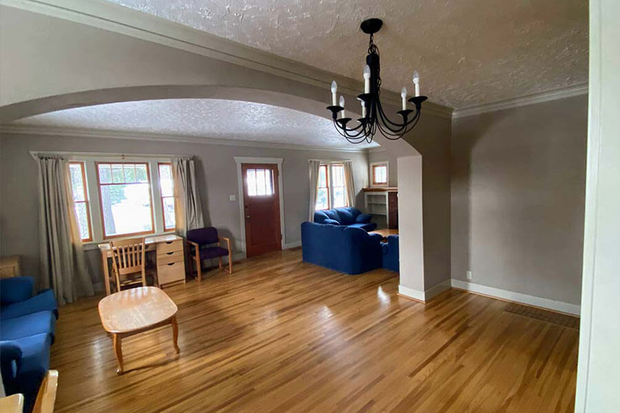 Spacious, well-lit living and dining room with wooden floors, blue sofas, a wooden desk and a chandelier.