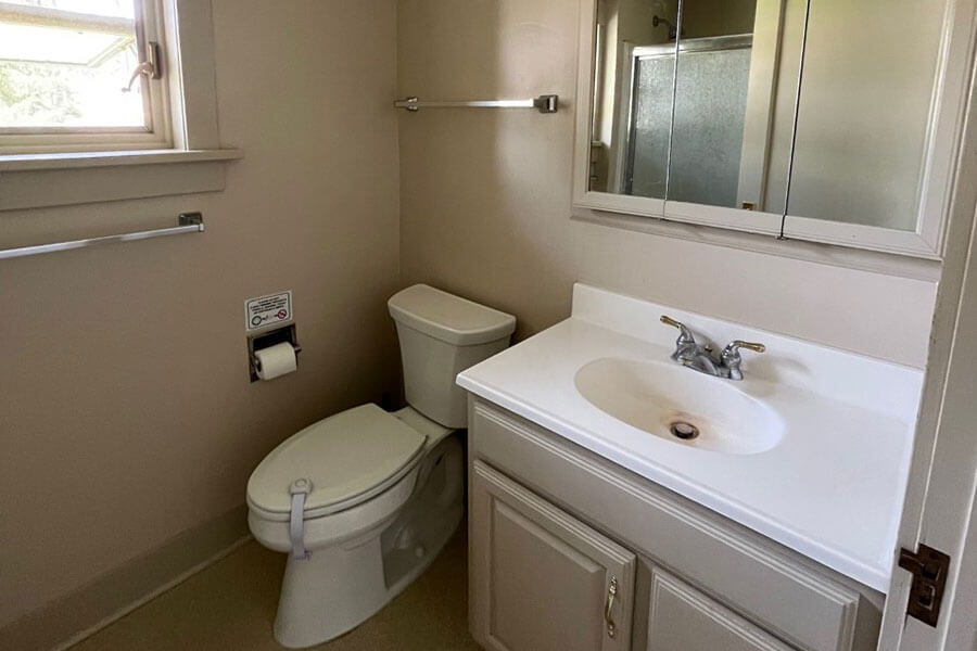 Tidy white and beige bathroom with toilet, sink, mirrored cabinet and shower with glass door.