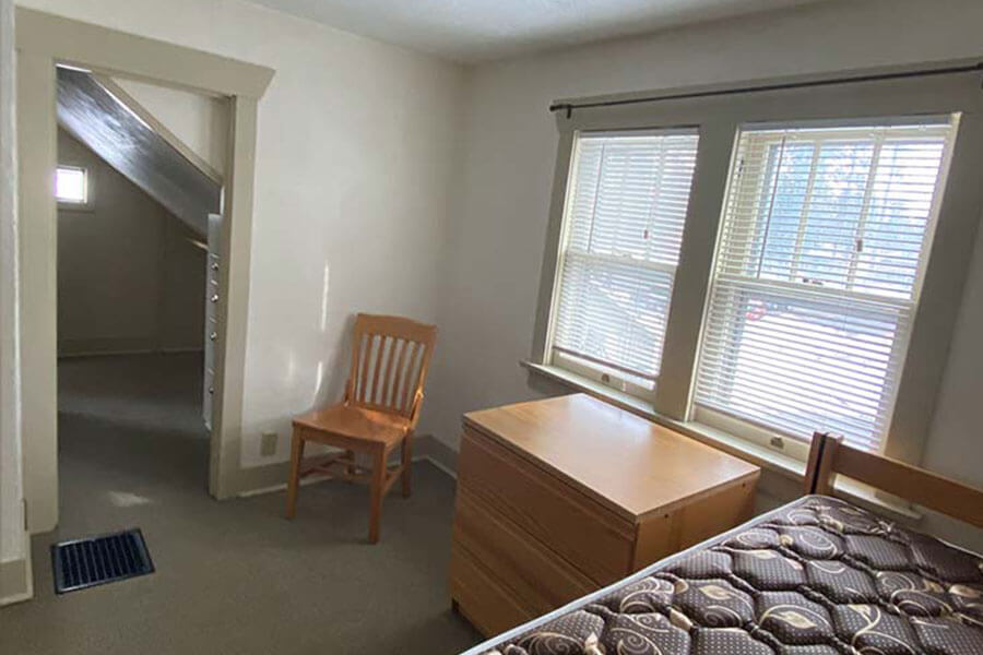 Classic bedroom with wooden furniture, single bed and large windows. Doorway leads to a small adjacent space.