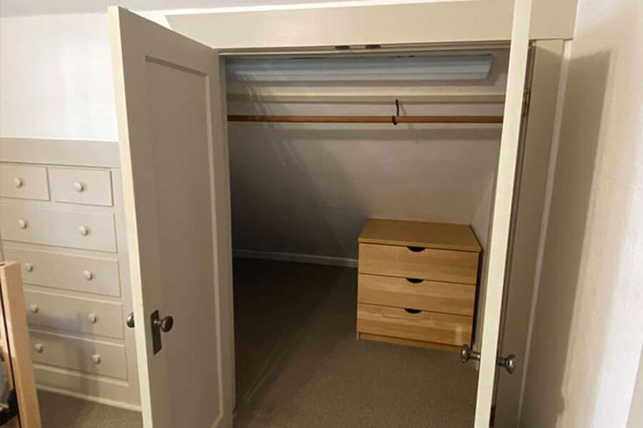 Open closet with a set of wooden drawers and a hanging rod, in a small alcove, adjacent to built-in drawers.