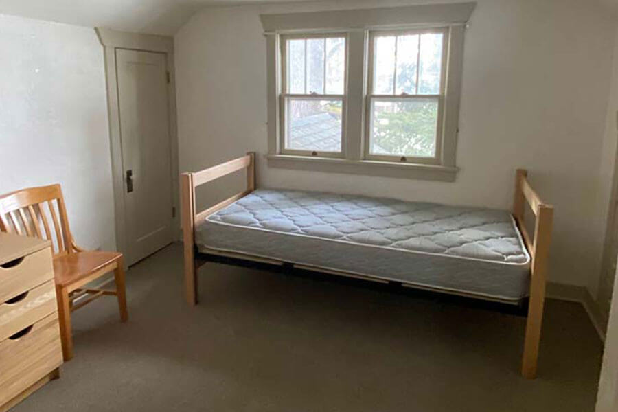 Classic bedroom with wooden furniture and a single bed. Large wood-framed windows let in natural light.