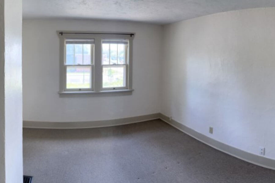 Empty room with white walls, beige carpet and a window overlooking the lawn and street.