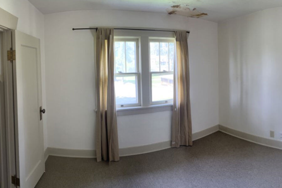 Empty room with large, curtained windows, white walls and beige carpet.