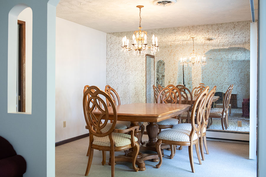 Elegant dining room with a wooden table, ornate chairs and a mirrored wall reflecting a chandelier.