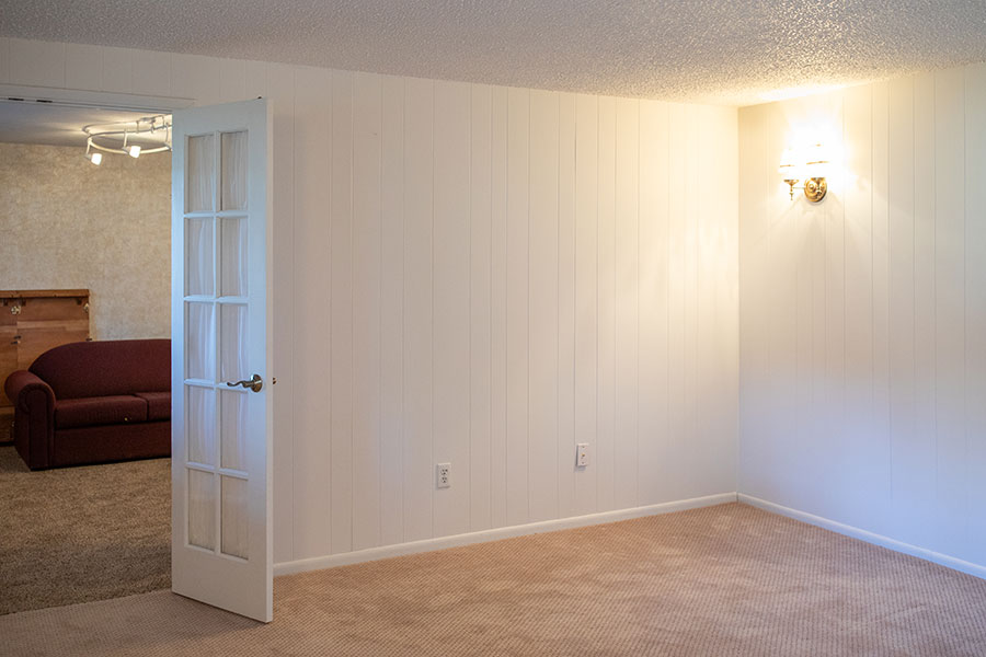 Classic bedroom with white paneled walls, wall sconce, and open French doors revealing a red sofa in the next room.