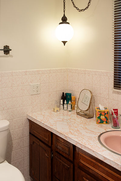 Vintage bathroom with a pink marble countertop, wooden cabinets and an elegant pendant lamp.