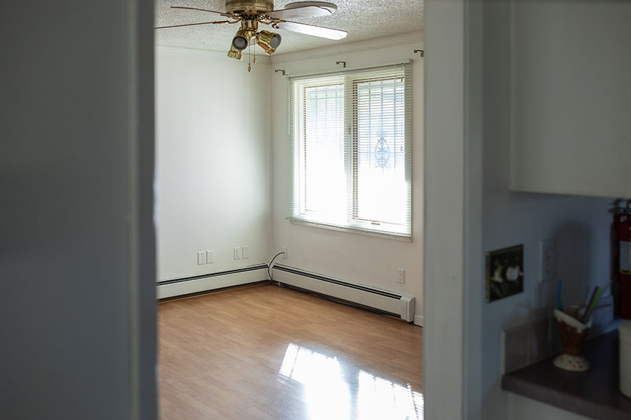 Small dining room with wooden floors, white walls, large windows and a ceiling fan.