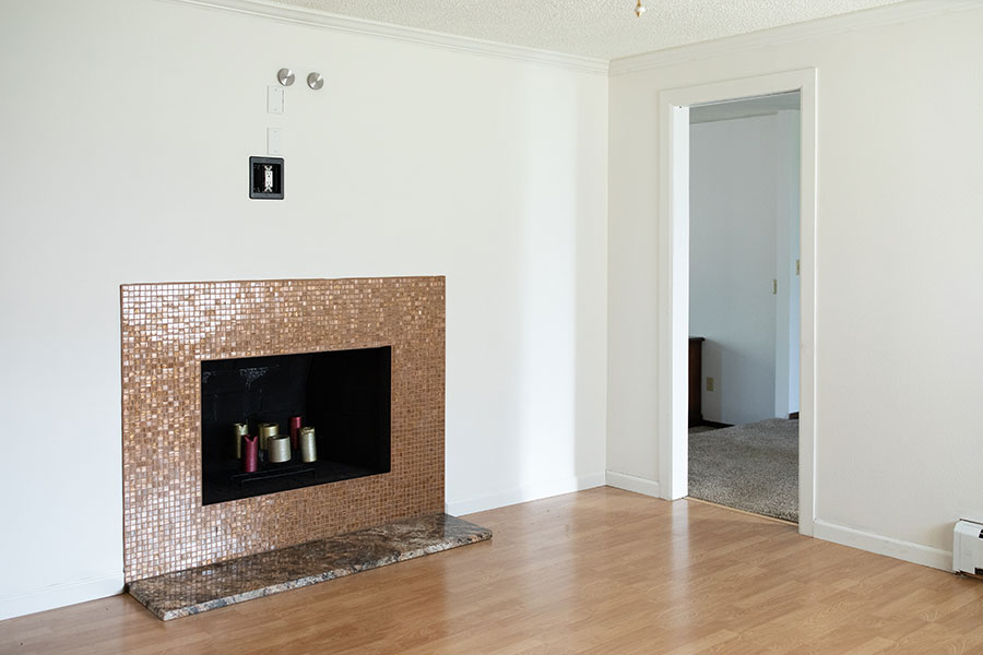 Small living room with wood floors, a tiled fireplace with candles inside and a doorway leading to a carpeted area.