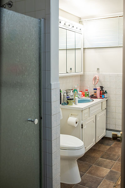 White-tiled bathroom complete with a shower, toilet, sink and cabinetry.