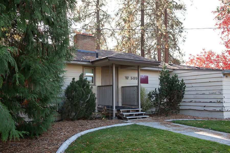 Single-story rambler set among stately pines with evergreen shrubs near the entry.