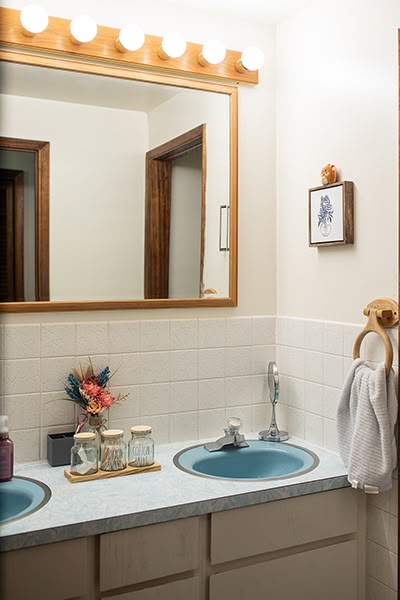 Tidy bathroom with twin blue sinks, white tile and a large mirror with good lighting.