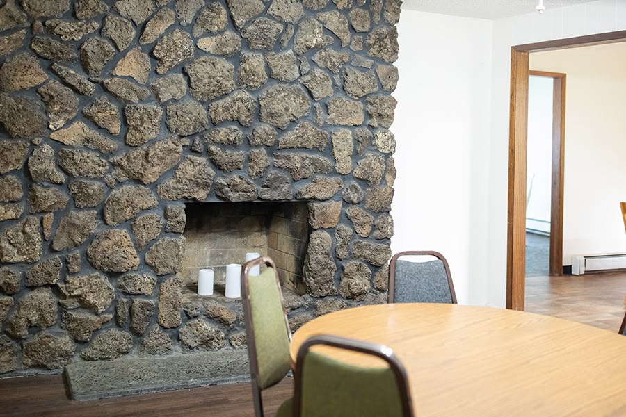 An open living space with a stone fireplace and a round wooden table and chairs.