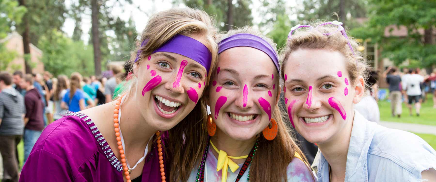 Three students, with headbands and bright face paint, stand close together and smile.