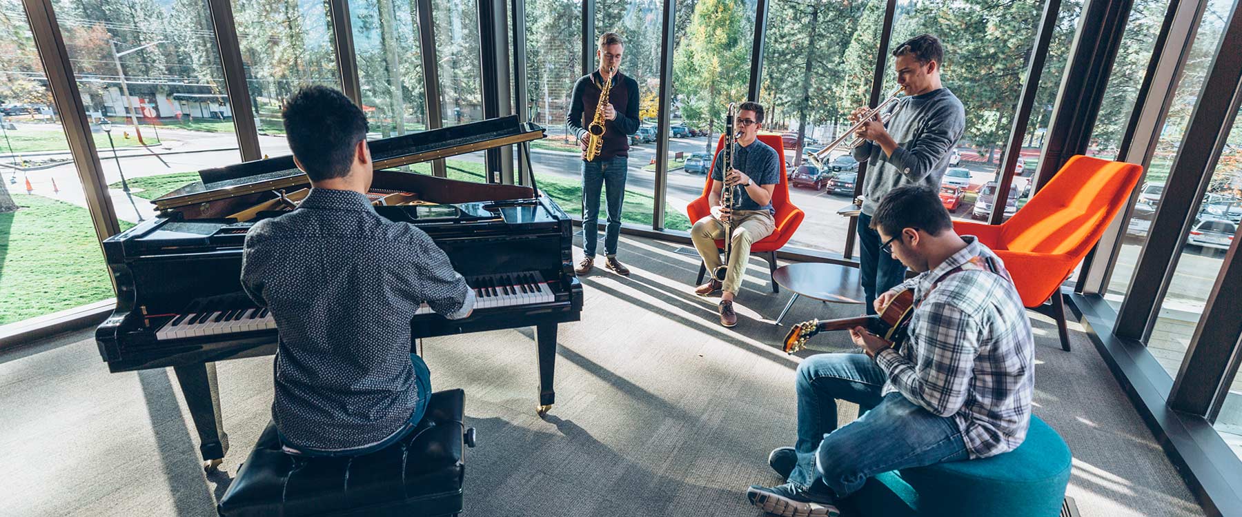 Five musicians in a sunlit room, playing piano, saxophone, trumpet, clarinet and guitar, seated by large windows.