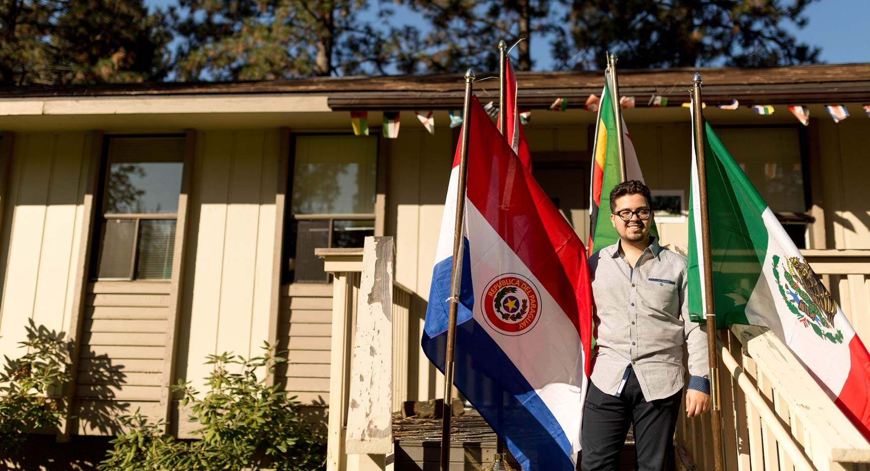 Roland Beaz stands with four international flags, including the Republic of Paraguay flag, on a sunny day.