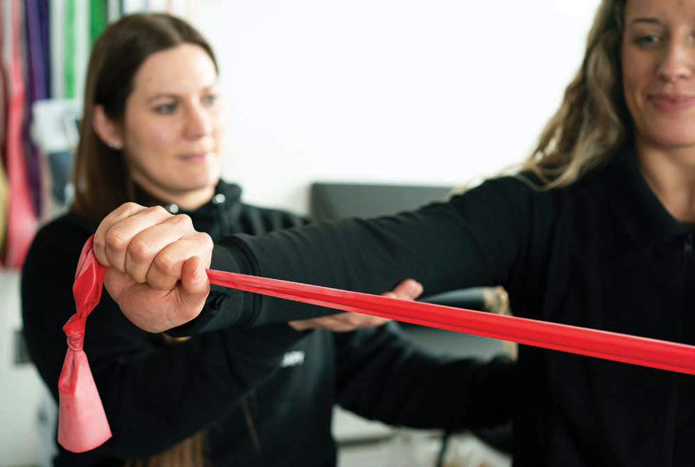 McClammer demonstrates teaching a shoulder strengthening exercise to a classmate using a red resistance band.