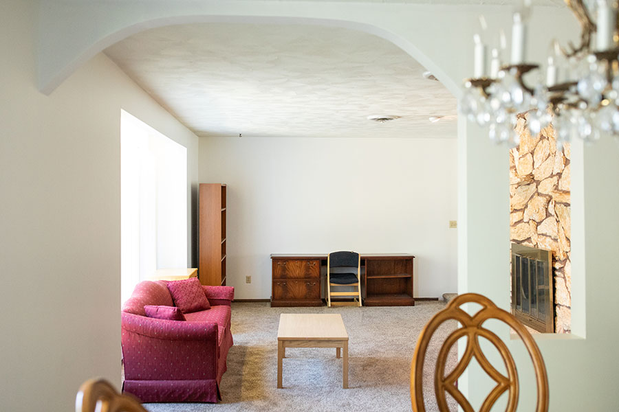 Living room with red sofa, a large fireplace and large windows. Archway opens to dining area with chandelier.