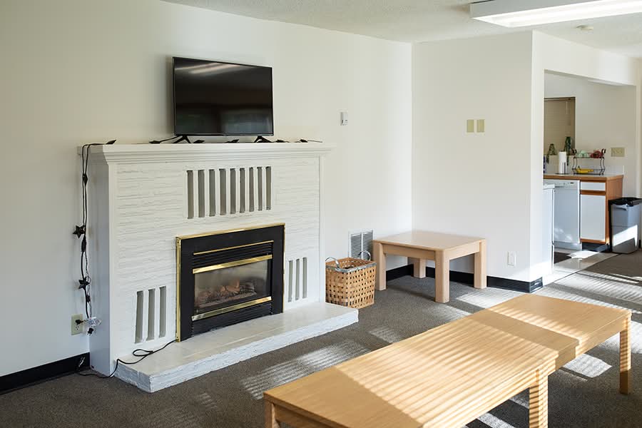 A TV hangs above a white brick fireplace with gas insert in a well-lit living room with multiple tables.