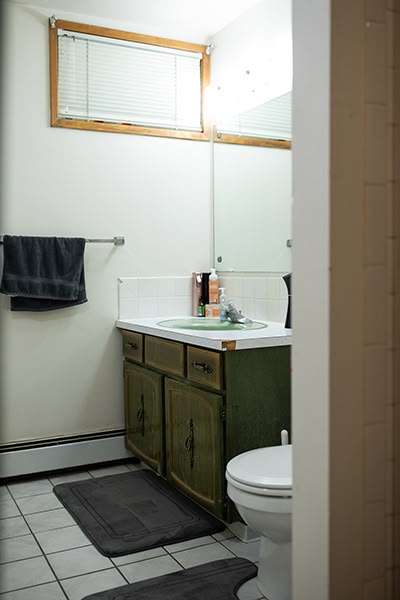 Bathroom with tiled floor, dark green vanity, and daylight window with blinds.