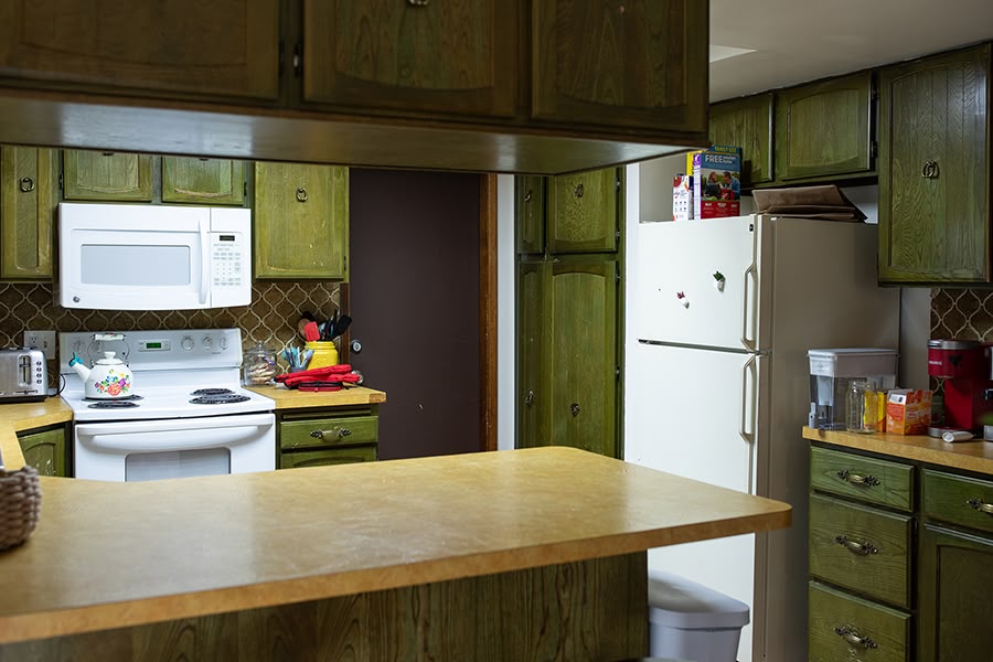 A cozy kitchen with green cabinets and tiled backsplashes, viewed from the kitchen nook area.