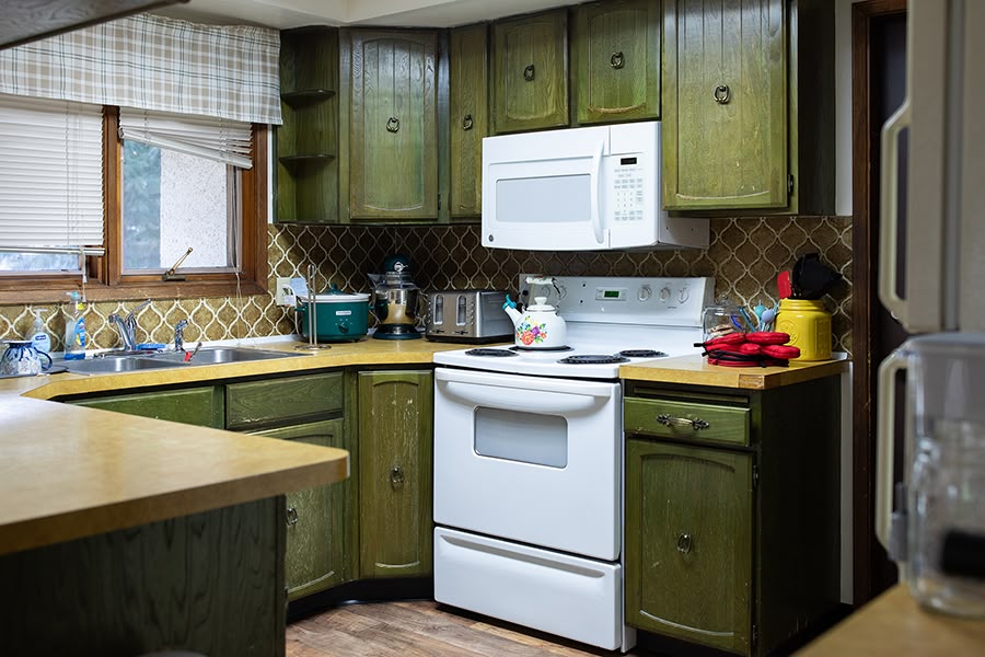 A cozy kitchen with green cabinets, a white stove and microwave, and various appliances on the countertop.