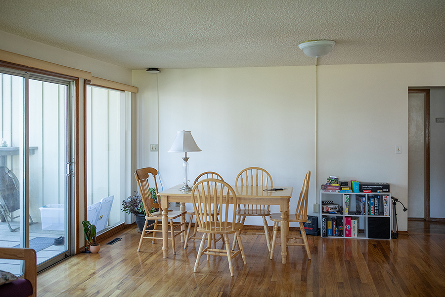 Large dining room with wooden floors, a table and four chairs, and a shelf of board games. The view through sliding glass doors is of a large deck.