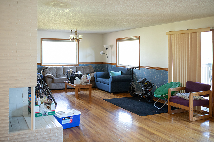 Spacious living room with wood floors, a large stone fireplace, and multiple sofas and chairs. Sliding glass doors and large windows let in natural light.