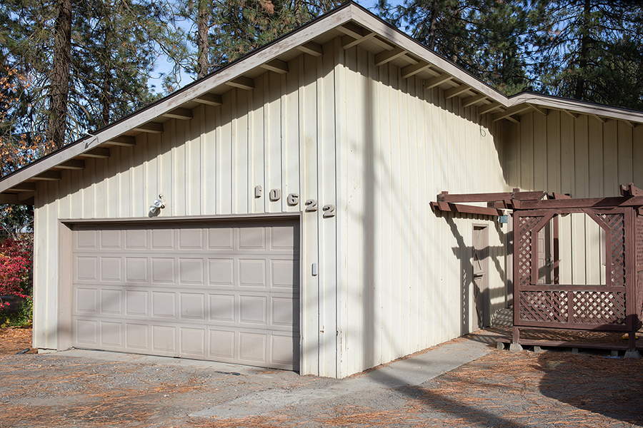 A single-story, tan-colored house with an angled roof over the garage and a front porch with wooden trellises.